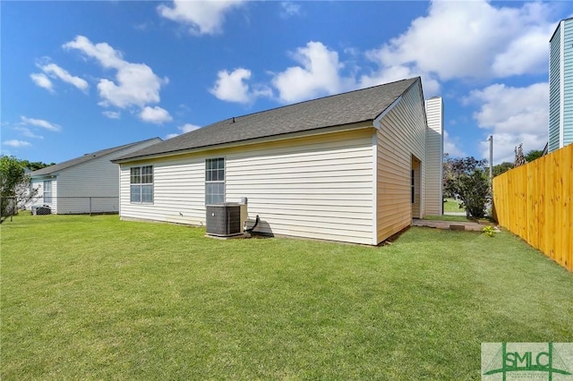 rear view of house with a yard, central air condition unit, a shingled roof, and a fenced backyard