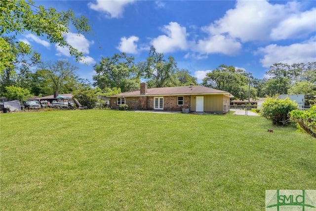back of property with a chimney, a yard, french doors, and fence