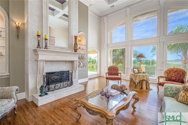 living area featuring wood finished floors, ornamental molding, a towering ceiling, baseboards, and a tiled fireplace