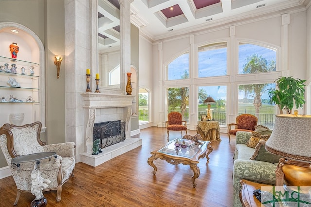 living area with wood finished floors, crown molding, coffered ceiling, a high ceiling, and a tile fireplace
