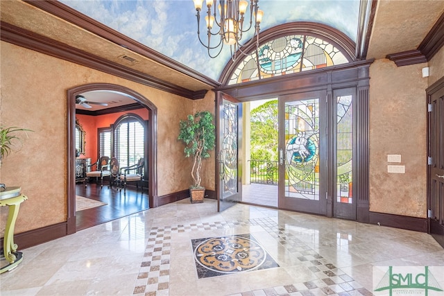 foyer entrance featuring a notable chandelier, baseboards, ornamental molding, arched walkways, and a textured wall