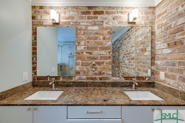 bathroom featuring double vanity, an enclosed shower, brick wall, and a sink