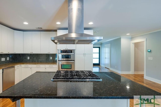 kitchen with baseboards, ornamental molding, decorative backsplash, island range hood, and appliances with stainless steel finishes