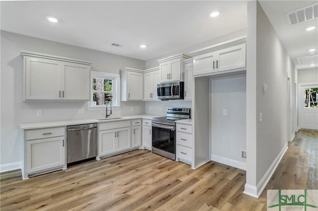 kitchen featuring light wood finished floors, a sink, stainless steel appliances, visible vents, and light countertops