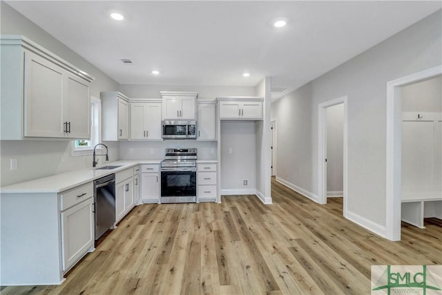 kitchen with light wood-style flooring, stainless steel appliances, a sink, white cabinetry, and light countertops