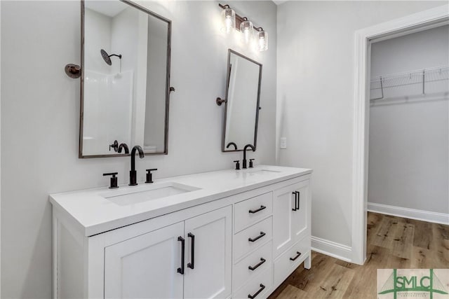 full bath featuring double vanity, wood finished floors, baseboards, and a sink