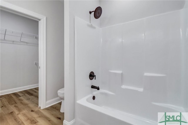 bathroom with toilet, wood finished floors, a spacious closet, bathing tub / shower combination, and baseboards