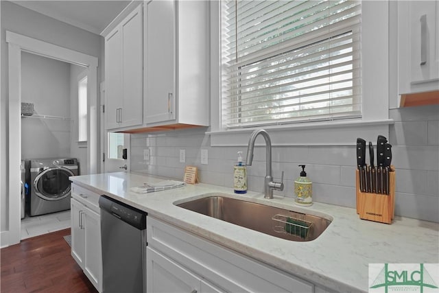 kitchen featuring independent washer and dryer, stainless steel dishwasher, a sink, white cabinetry, and backsplash