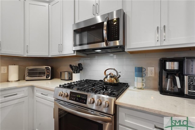 kitchen with a toaster, light stone counters, decorative backsplash, white cabinets, and appliances with stainless steel finishes