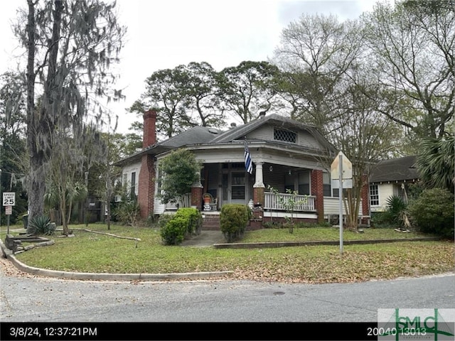 view of front of house with a chimney, brick siding, a front yard, and covered porch