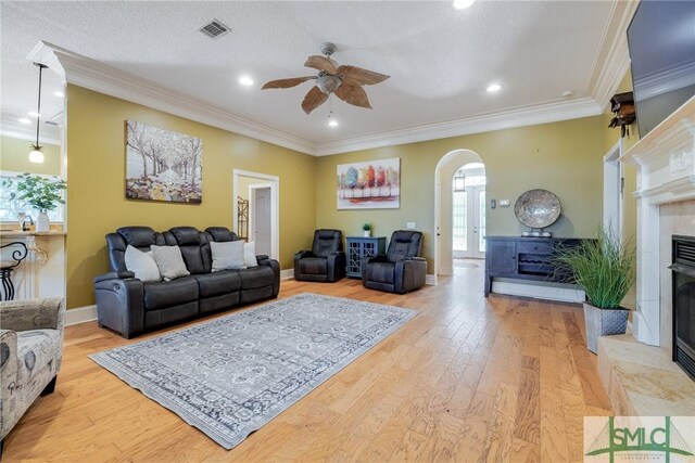 living room featuring wood finished floors, visible vents, a fireplace, ceiling fan, and arched walkways
