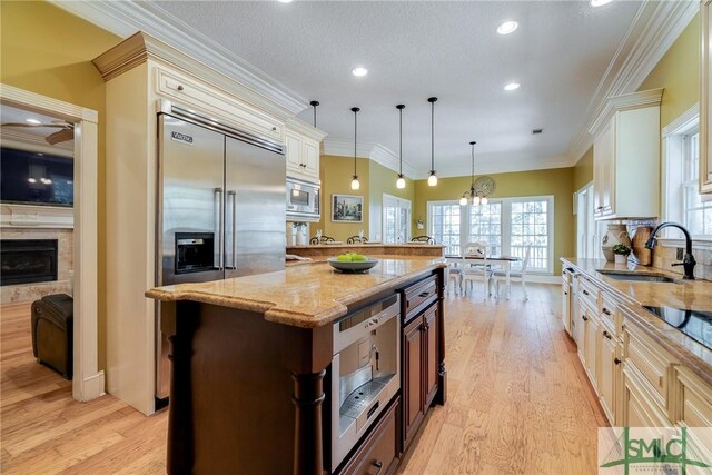 kitchen featuring a sink, built in appliances, light wood-style flooring, and light stone countertops