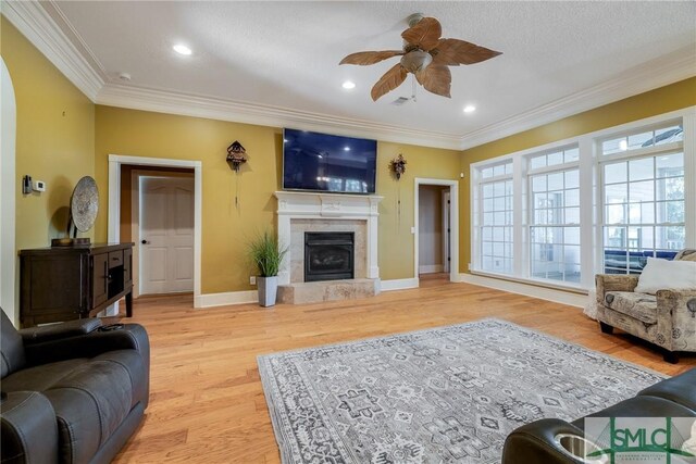 living room featuring a ceiling fan, a fireplace with raised hearth, baseboards, ornamental molding, and light wood-type flooring