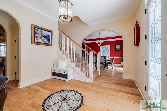 foyer entrance with ornamental molding, light wood-style floors, a chandelier, and arched walkways