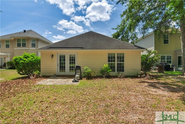 rear view of property with a shingled roof, a patio area, and a lawn