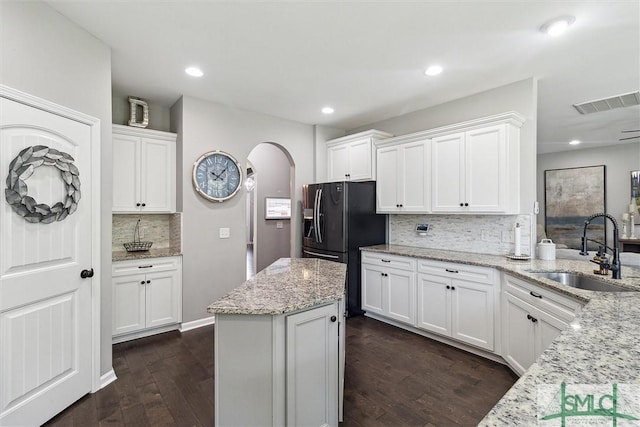 kitchen featuring backsplash, white cabinets, a sink, and arched walkways