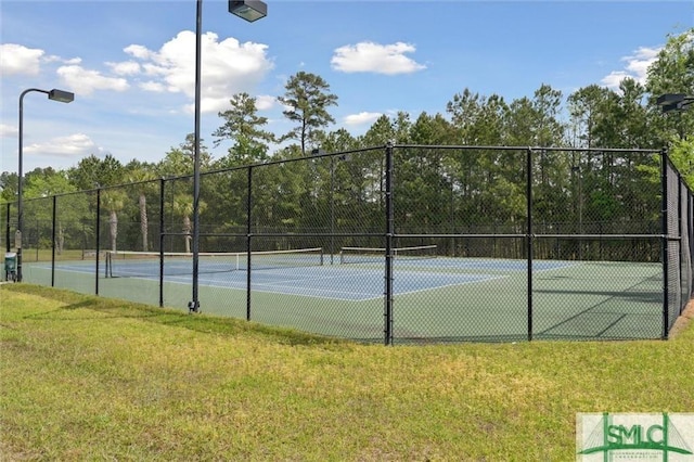 view of tennis court with a lawn and fence