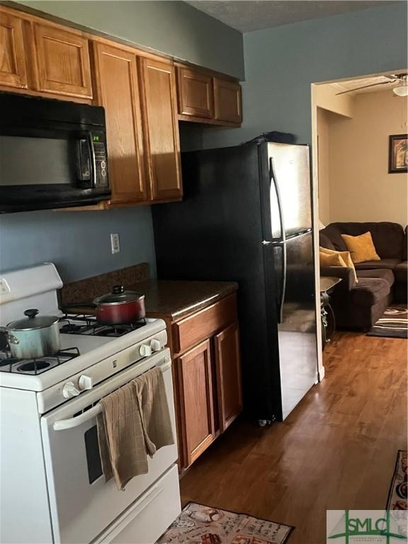 kitchen featuring dark countertops, brown cabinets, black appliances, and dark wood finished floors