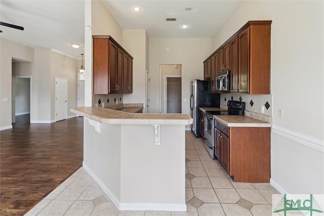 kitchen with visible vents, light tile patterned flooring, a peninsula, backsplash, and appliances with stainless steel finishes