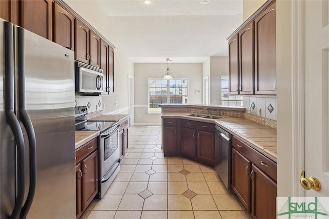 kitchen featuring pendant lighting, a sink, decorative backsplash, tile counters, and stainless steel appliances