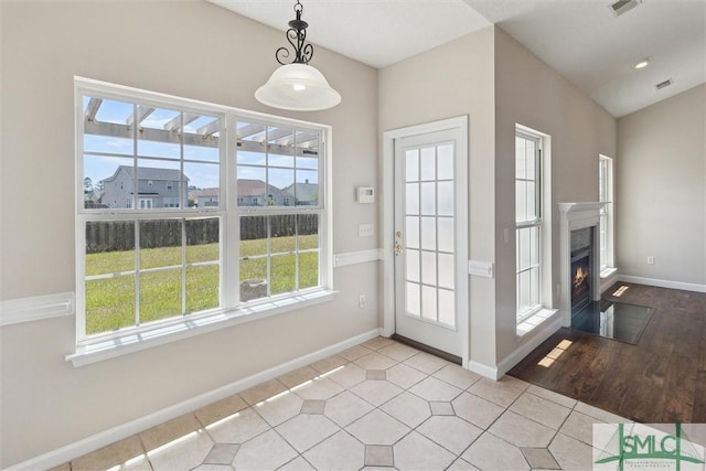 doorway to outside featuring light tile patterned floors, visible vents, baseboards, and a fireplace with flush hearth