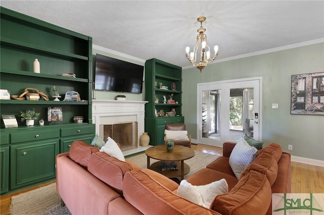 living room featuring a chandelier, ornamental molding, a fireplace with raised hearth, light wood finished floors, and baseboards