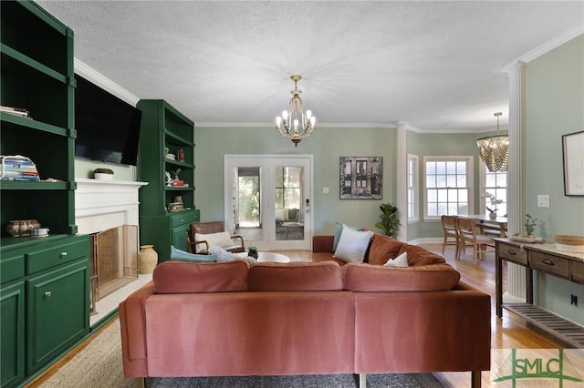 living room with a chandelier, ornamental molding, light wood-style flooring, a fireplace with raised hearth, and a textured ceiling