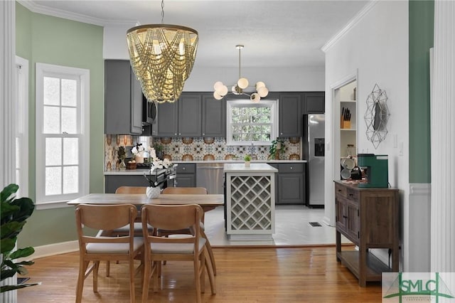 kitchen with a chandelier, gray cabinets, stainless steel appliances, crown molding, and tasteful backsplash