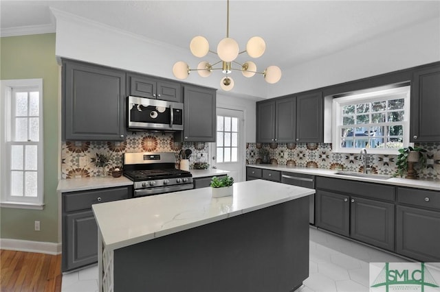 kitchen with appliances with stainless steel finishes, a sink, gray cabinets, decorative backsplash, and ornamental molding