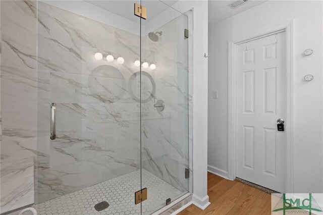 full bath with a marble finish shower and wood finished floors