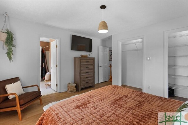 bedroom featuring light wood-type flooring, two closets, baseboards, and connected bathroom