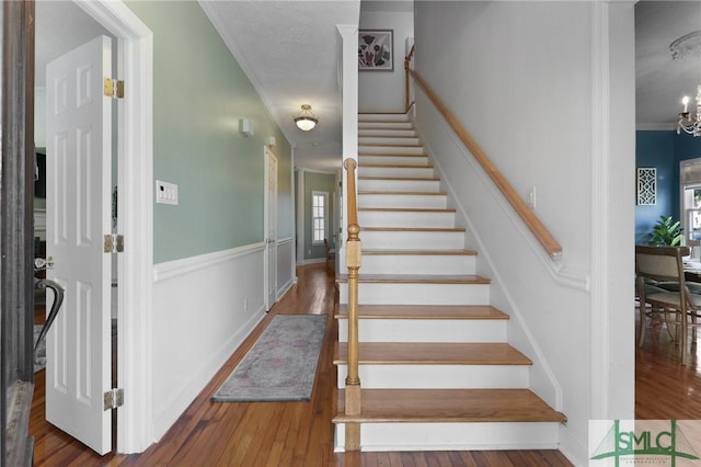 staircase featuring crown molding, wood finished floors, a chandelier, and baseboards