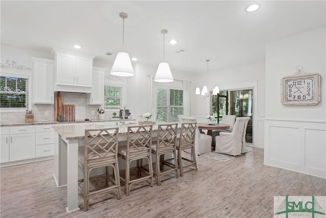 195 Wildlife View Ct N, Richmond Hill, GA 31324 - kitchen featuring white cabinets, light stone countertops, light wood-type flooring, backsplash, and a decorative wall