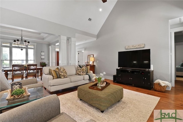 living room with decorative columns, wood finished floors, a chandelier, baseboards, and crown molding