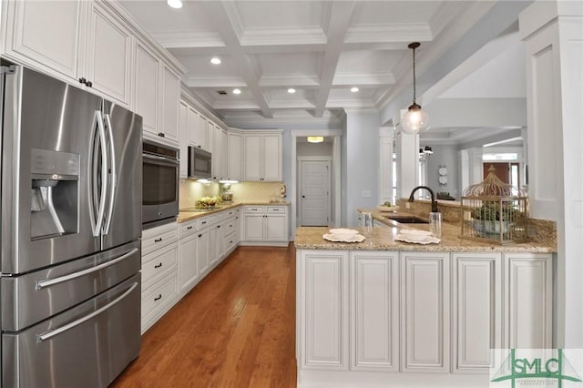 kitchen featuring appliances with stainless steel finishes, a sink, beamed ceiling, a peninsula, and light wood finished floors