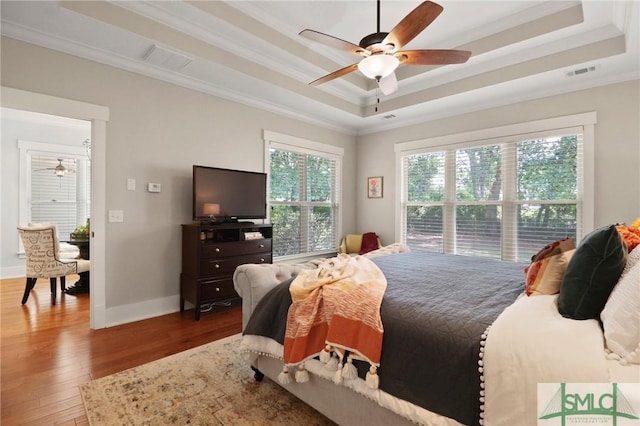 bedroom with a tray ceiling, ornamental molding, wood finished floors, baseboards, and a ceiling fan