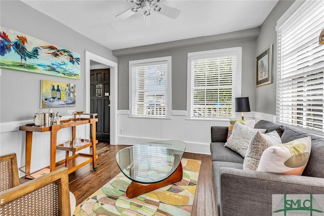 living area with a ceiling fan, wood finished floors, and wainscoting