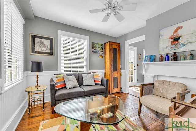 living room featuring a wainscoted wall, wood-type flooring, and a ceiling fan