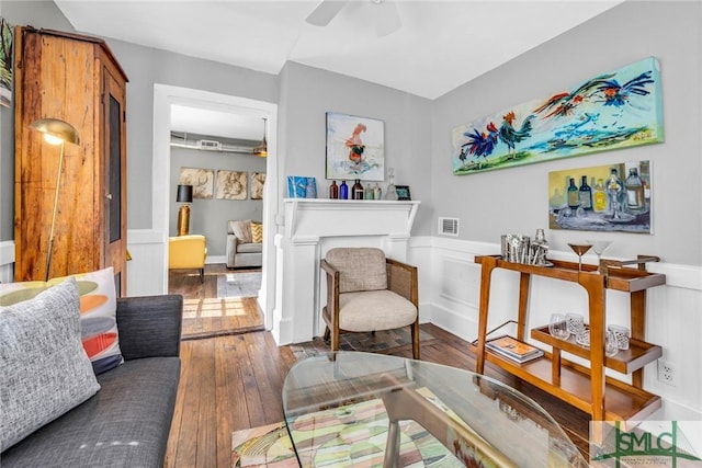 living area featuring wood-type flooring, a ceiling fan, and a wainscoted wall