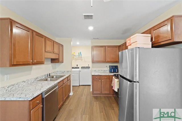 kitchen featuring appliances with stainless steel finishes, washer and clothes dryer, light wood finished floors, a sink, and brown cabinetry