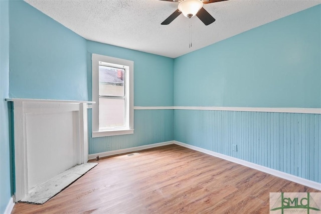 empty room with wood finished floors, a ceiling fan, baseboards, and a textured ceiling