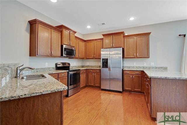 901 Garden Hills Loop, Richmond Hill, GA 31324 - kitchen with appliances with stainless steel finishes, a peninsula, a sink, light wood-style flooring, and light stone counters