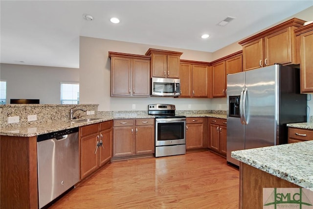 901 Garden Hills Loop, Richmond Hill, GA 31324 - kitchen with stainless steel appliances, a sink, a peninsula, light wood-style flooring, and brown cabinets