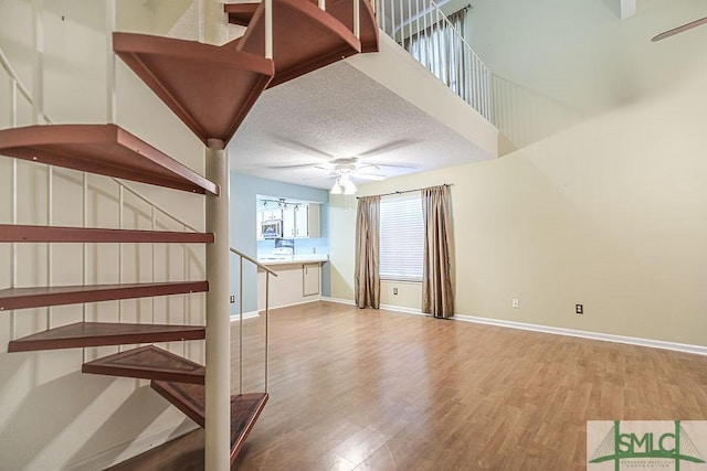 stairway featuring ceiling fan, wood finished floors, baseboards, and a textured ceiling