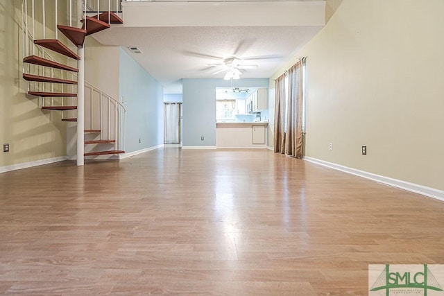 unfurnished living room featuring stairs, a ceiling fan, light wood-style flooring, and baseboards