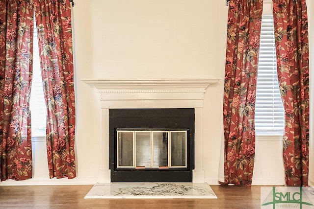 detailed view of wood finished floors, a glass covered fireplace, and baseboards