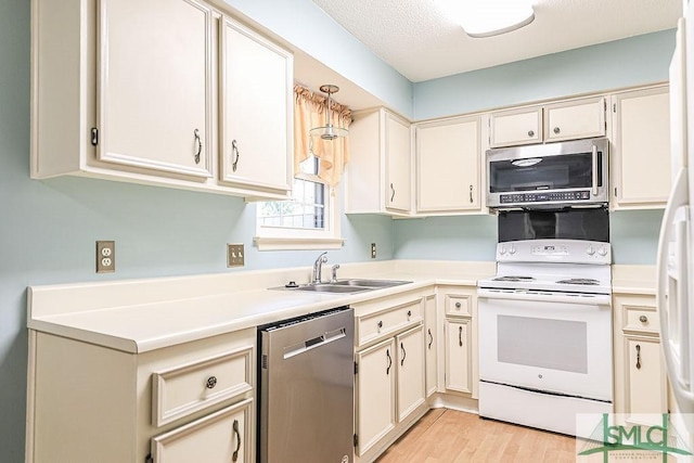 kitchen featuring appliances with stainless steel finishes, a sink, light countertops, light wood finished floors, and cream cabinetry
