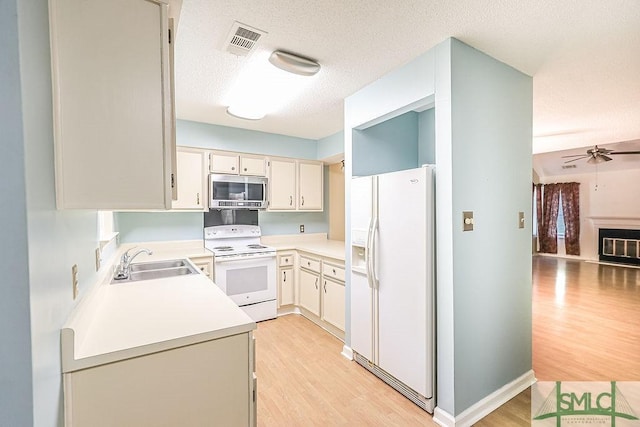 kitchen with white appliances, a sink, light wood finished floors, ceiling fan, and light countertops
