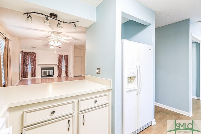 kitchen featuring white fridge with ice dispenser, a glass covered fireplace, a ceiling fan, light countertops, and light wood-style flooring