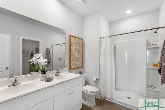 bathroom featuring a stall shower, toilet, double vanity, and wood finished floors